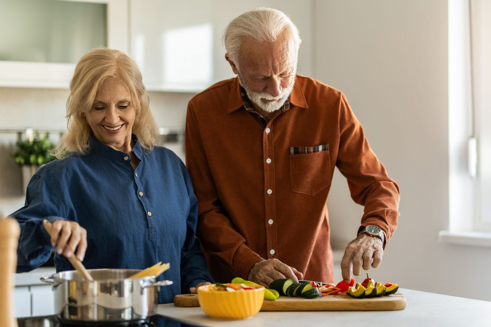Older couple preparing a nutrient-dense whole food plant-based meal together in a bright kitchen.