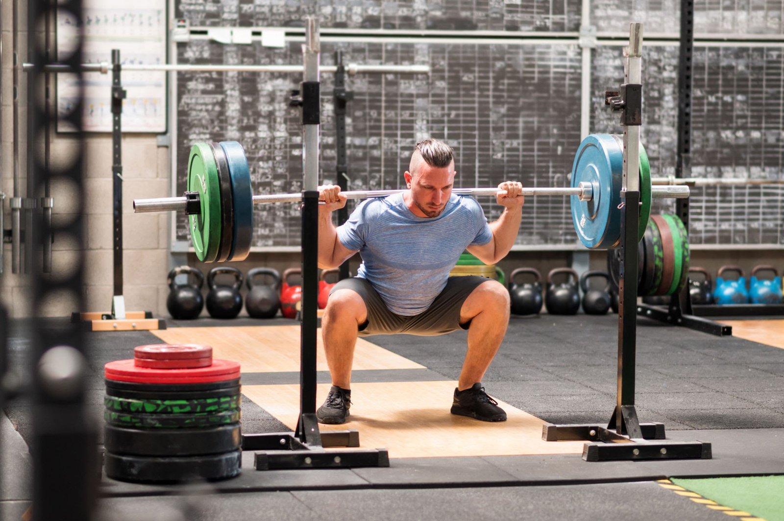 Full body of determined male athlete in sportswear doing back squats with heavy barbell during intense workout in gym
