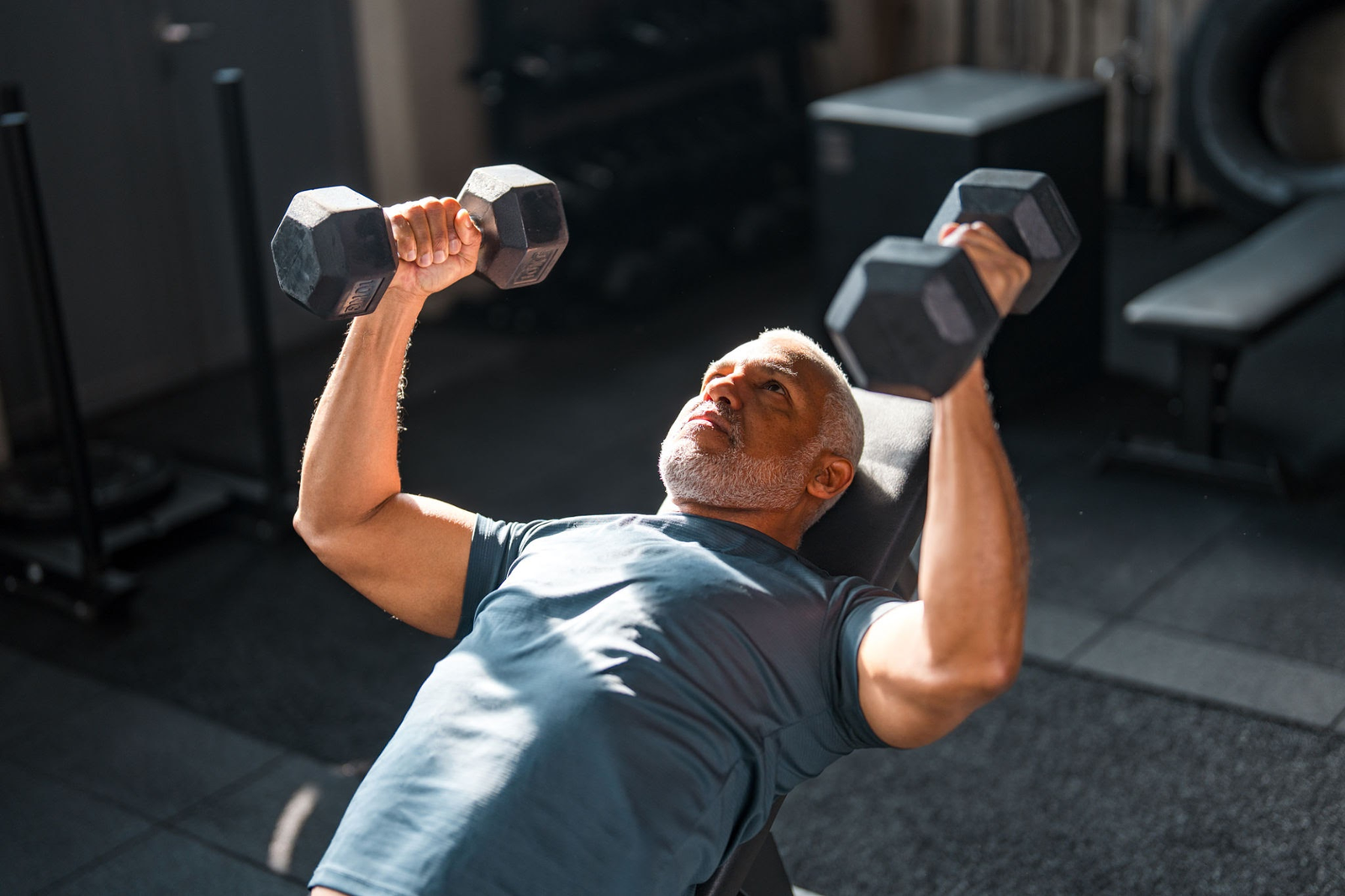 Focused mature male athlete in his 50s performing an incline dumbbell press in a gym setting, demonstrating resistance training to overcome muscle anabolic resistance and preserve lean muscle mass.